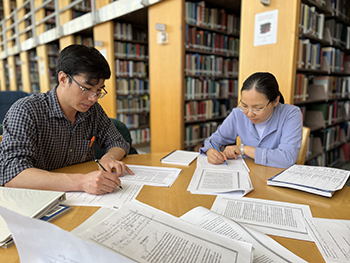 A man and woman study at a library table